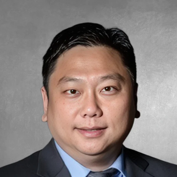 Close-up headshot of a man in a dark suit and light blue shirt, neutral background