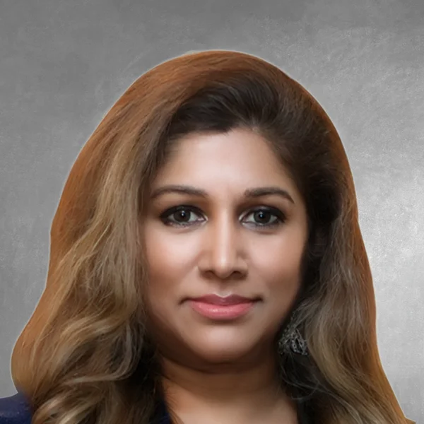 Portrait of a woman with light brown, wavy hair and subtle makeup looking at the camera in a neutral studio setting.