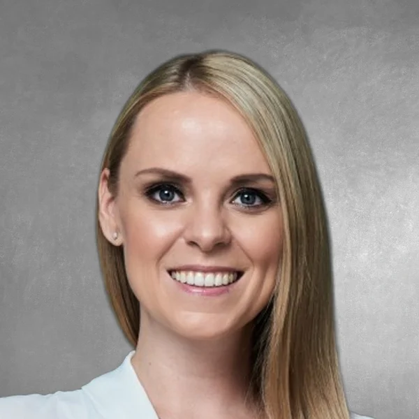 Portrait of a smiling blonde woman with straight hair against a gray studio background, shoulders visible.